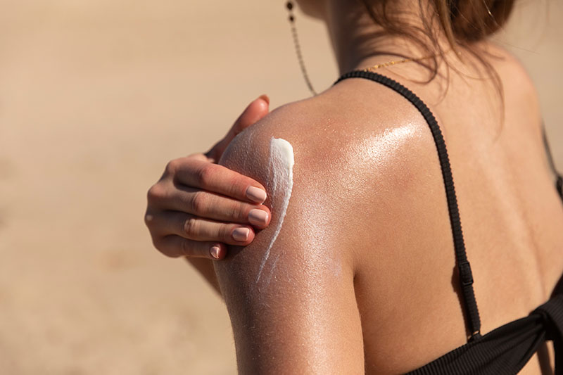 young woman applying sun cream on her shoulder